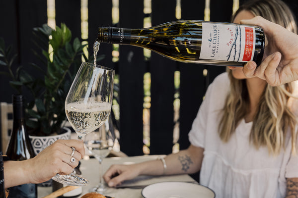 Person pouring wine from a bottle into a glass at a dining table.